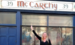 Karen McCarthy pointing at a Mc Carthy shop sign above her head